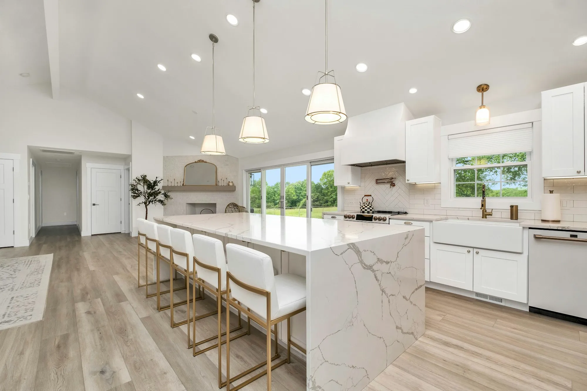 A large new kitchen with white cabinets, a marble island with bar stools and pendant lights