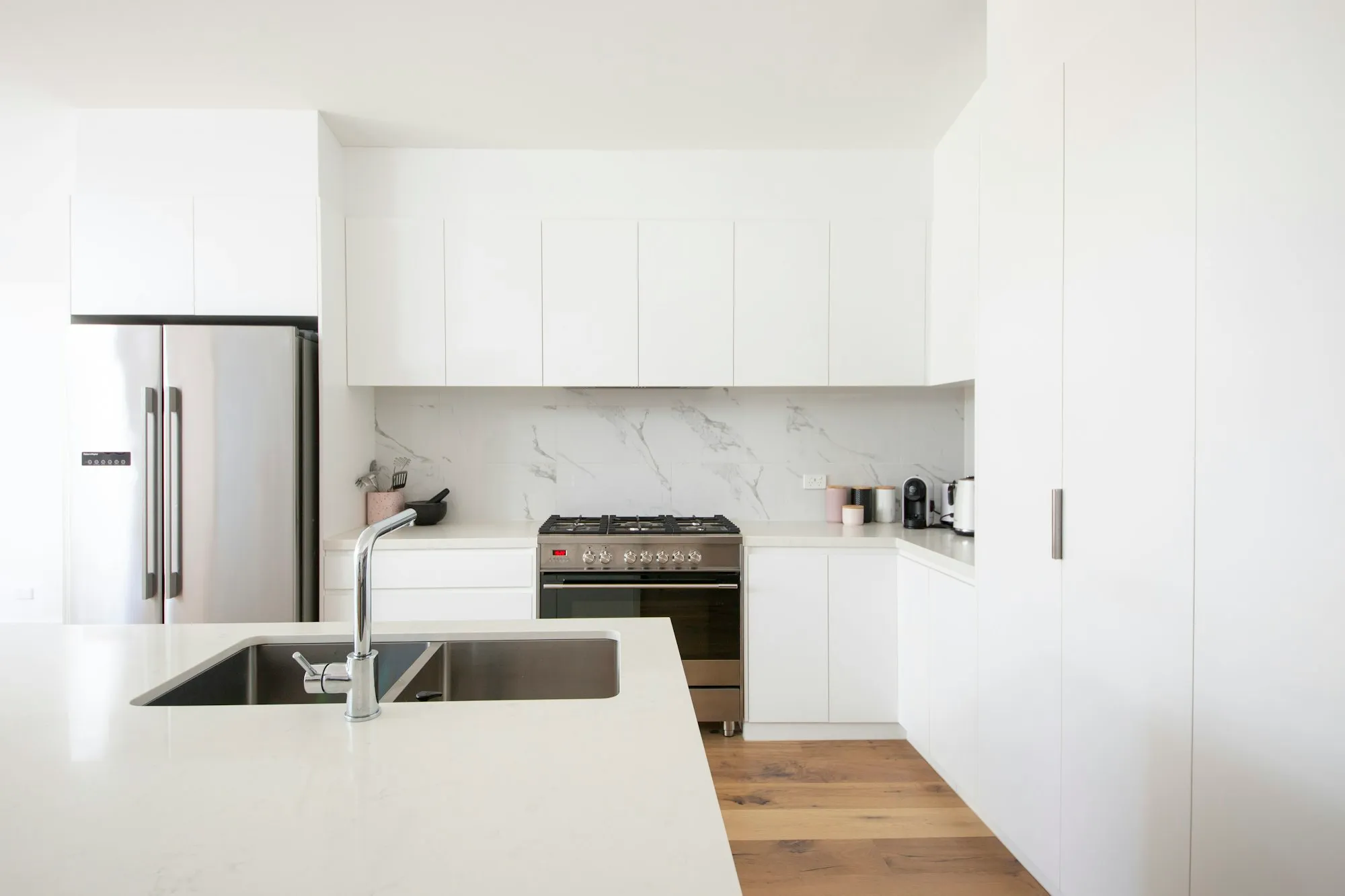 A white kitchen with flat panel doors, a marble look splashback and a stone benchtop