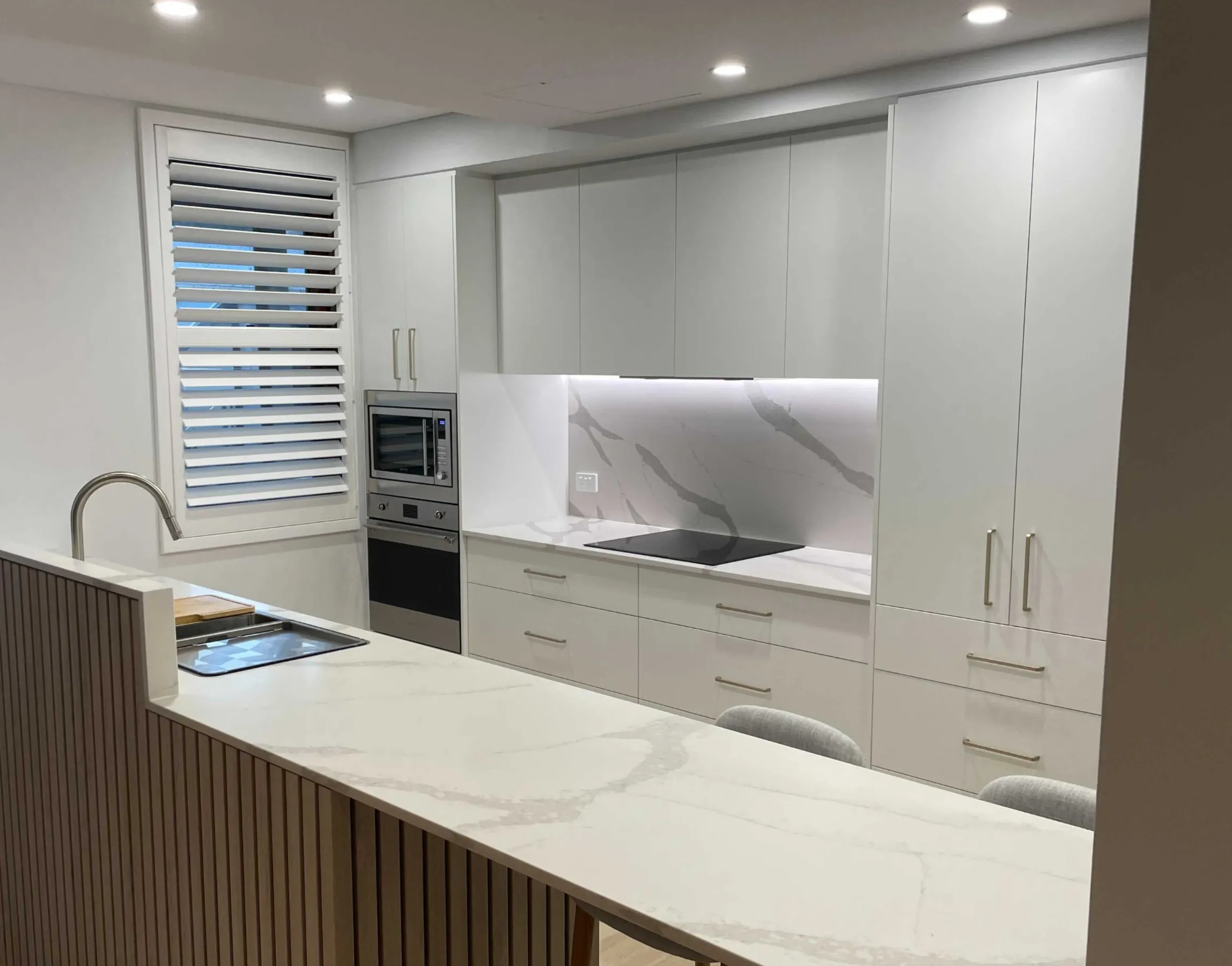 The same kitchen after the makeover, with white doors, a stone benchtop and brushed handles